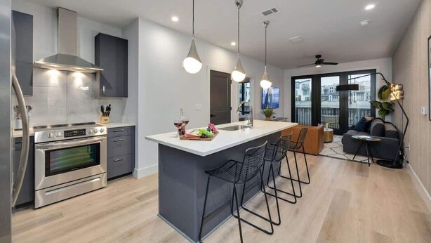 A modern kitchen with a central island, stainless steel appliances, pendant lighting, and a view to the outside.