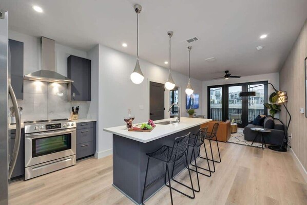 Una cocina moderna con una isla central, electrodomésticos de acero inoxidable, iluminación colgante y vistas al exterior.