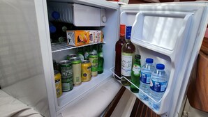 Un réfrigérateur rempli de boissons et d’en-cas, notamment des canettes, des bouteilles et un emballage de jus.