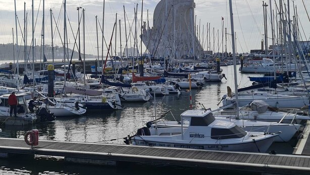 Un port de plaisance où sont amarrés de nombreux voiliers, un bâtiment imposant en arrière-plan et une jetée en bois avec une bouée de sauvetage.
