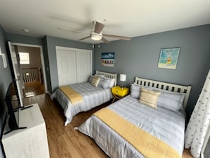 Quarto com duas camas, um ventilador de teto e uma porta que dá para outro cômodo.