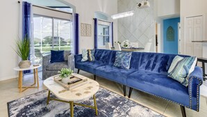 Un salon moderne avec un canapé bleu, une table basse ronde et une vue sur l’extérieur grâce à de grandes fenêtres.