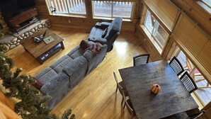 Interior acogedor de una cabaña con piso de madera, un sofá, un televisor, una mesa de comedor y un árbol de Navidad.