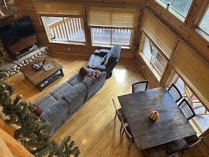Interior acogedor de una cabaña con piso de madera, un sofá, un televisor, una mesa de comedor y un árbol de Navidad.