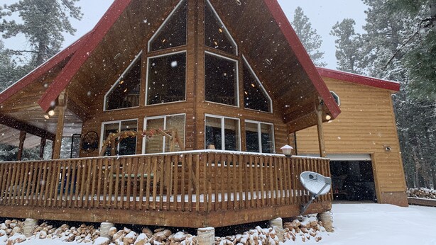 Una cabaña de madera con techo rojo y ventanas amplias, rodeada de nieve y árboles.