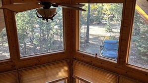 Una cabaña con ventanas amplias, un ventilador de techo y vistas al bosque circundante.
