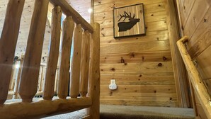 Una escalera de madera con barandilla, un interruptor de luz en la pared y una decoración de cabeza de ciervo enmarcada.