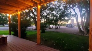 Un espacio al aire libre techado con pilares de madera y luces colgantes, césped y árboles.