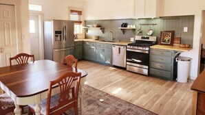 Una cocina moderna con comedor, que cuenta con electrodomésticos de acero inoxidable, sillas de madera y un ventilador de techo.