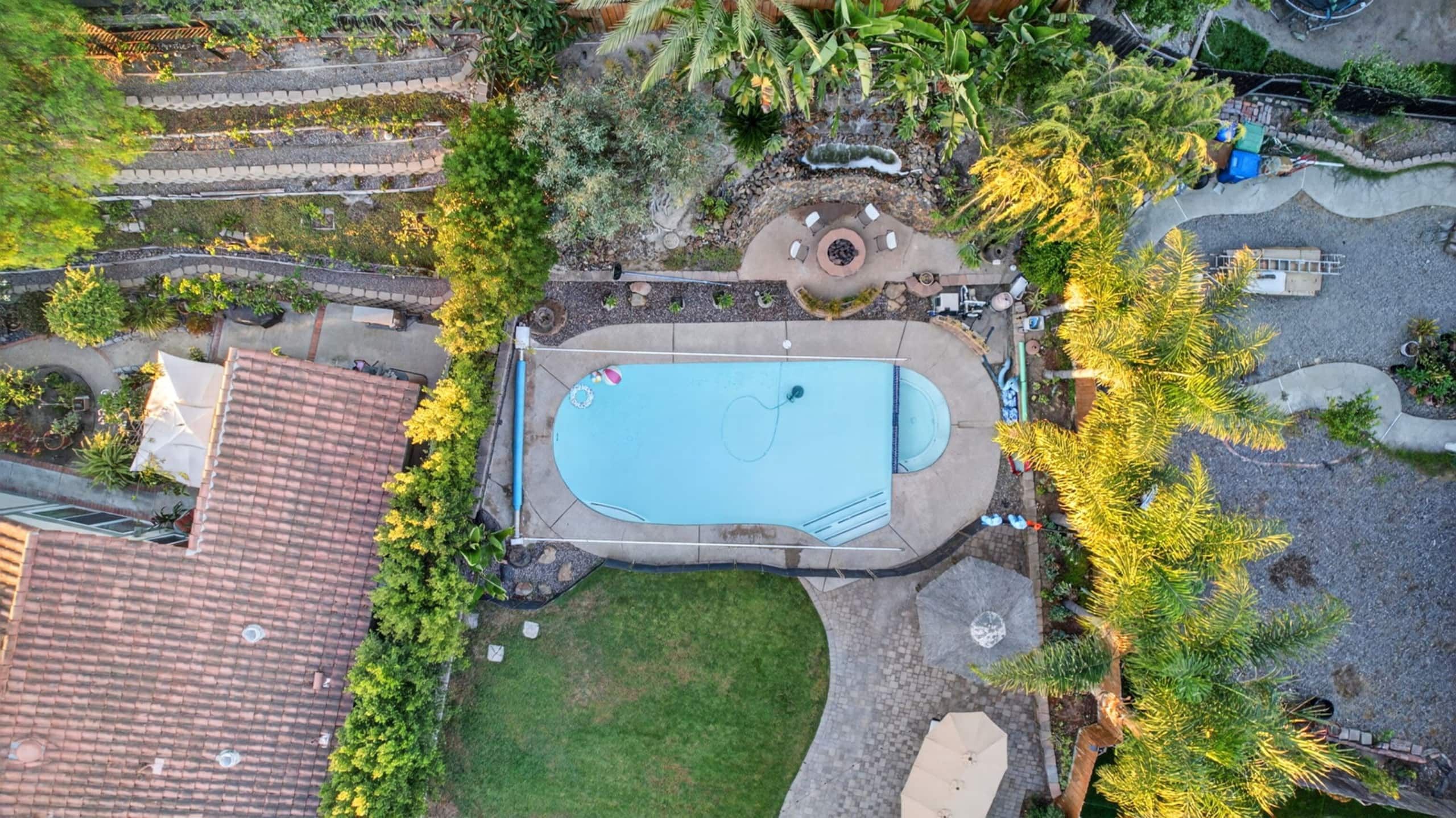 An aerial view of a residential property with a swimming pool, a patio area, and surrounding vegetation.