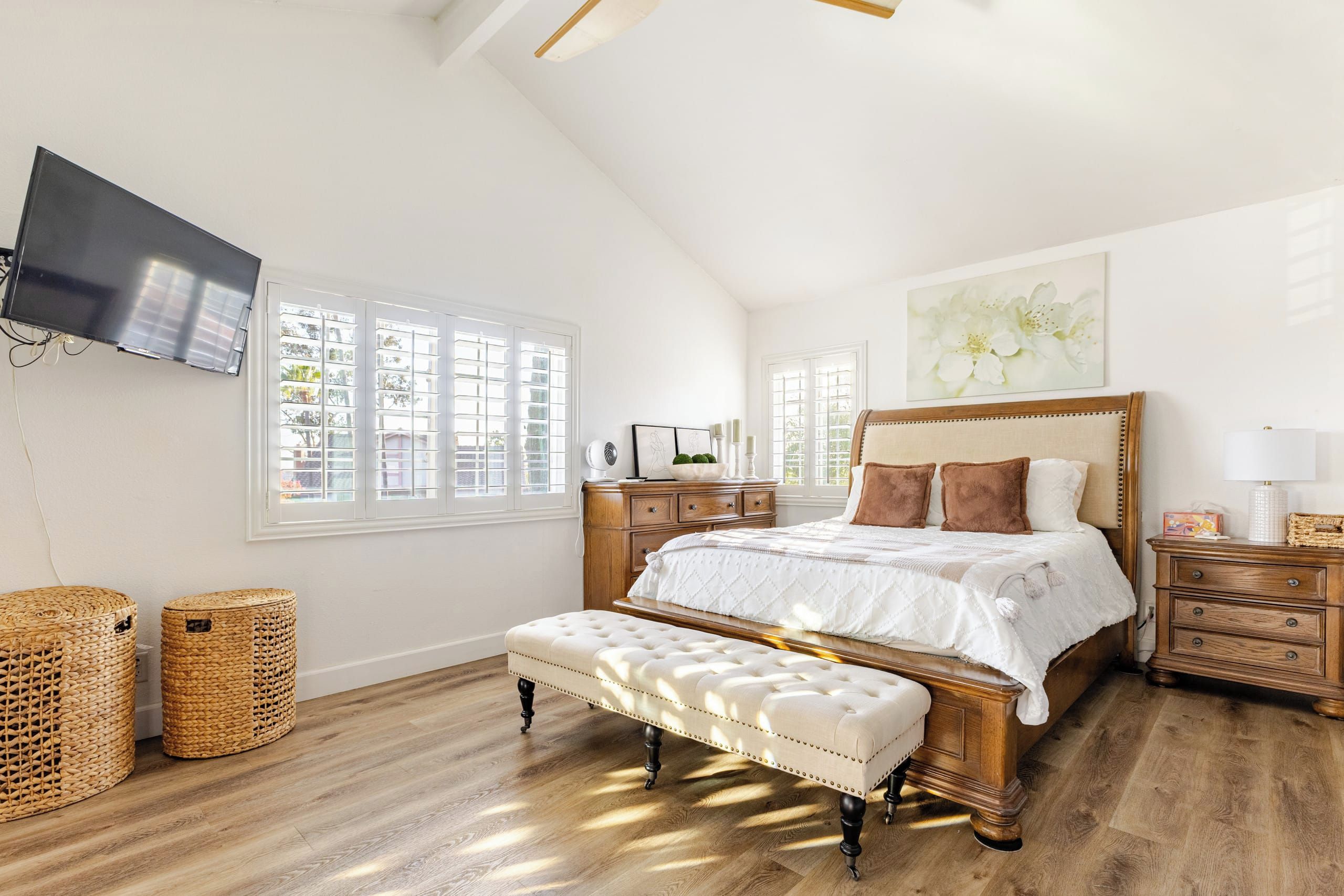 Un dormitorio con una cama grande, un televisor montado en la pared y una ventana con persianas.