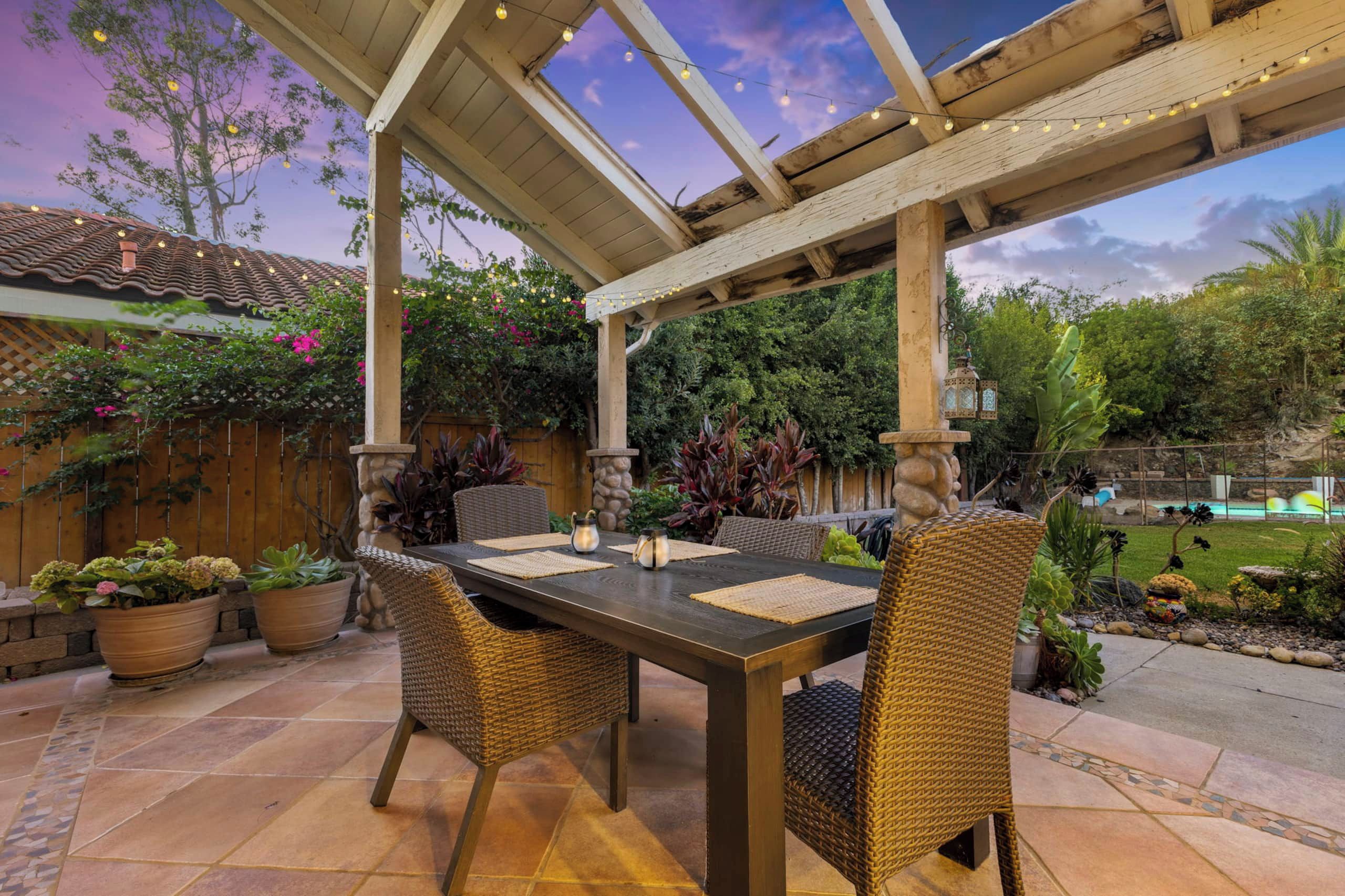 Une terrasse extérieure dotée d’une pergola, d’une table à manger, de chaises et de plantes en pot.