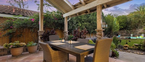 Eine Terrassengruppe im Freien mit einer Pergola, Esstisch, Stühlen und Topfpflanzen.