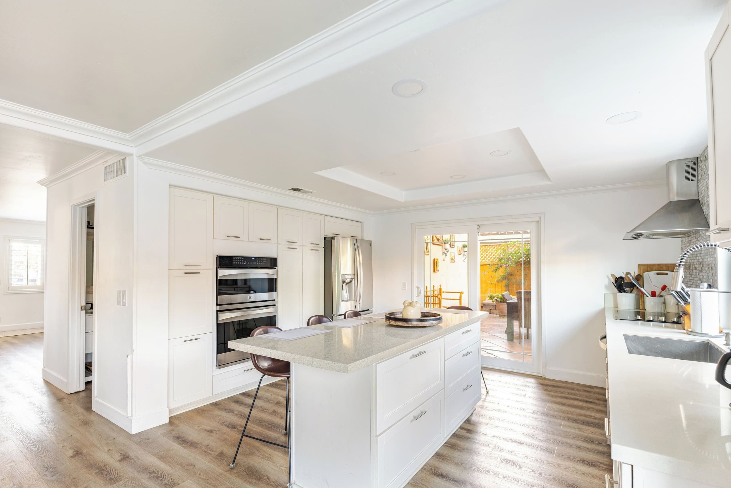 Una cocina amplia con muebles blancos, una isla central y vistas a un patio.