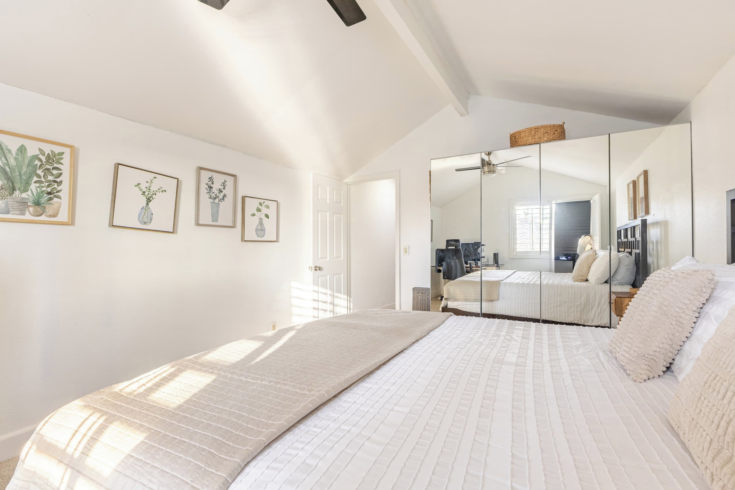 Un dormitorio con una cama grande, un armario, un espejo y tres impresiones botánicas enmarcadas en la pared.