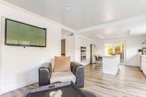 A modern living room with a leather sofa, a flat-screen TV, and a dining area with a kitchen in the background. - Spacious 4-bedroom suburban retreat in San Diego! Backyard, BBQ, Pool & Jacuzzi  (San Diego)
