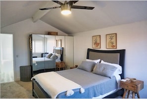 Ein Schlafzimmer mit Bett, Deckenventilator, Spiegel und Bildern an der Wand.