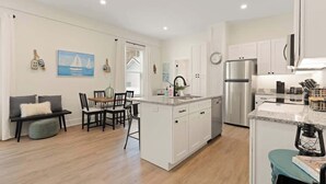Una cocina moderna con armarios blancos, un refrigerador de acero inoxidable y un comedor con mesa y sillas.