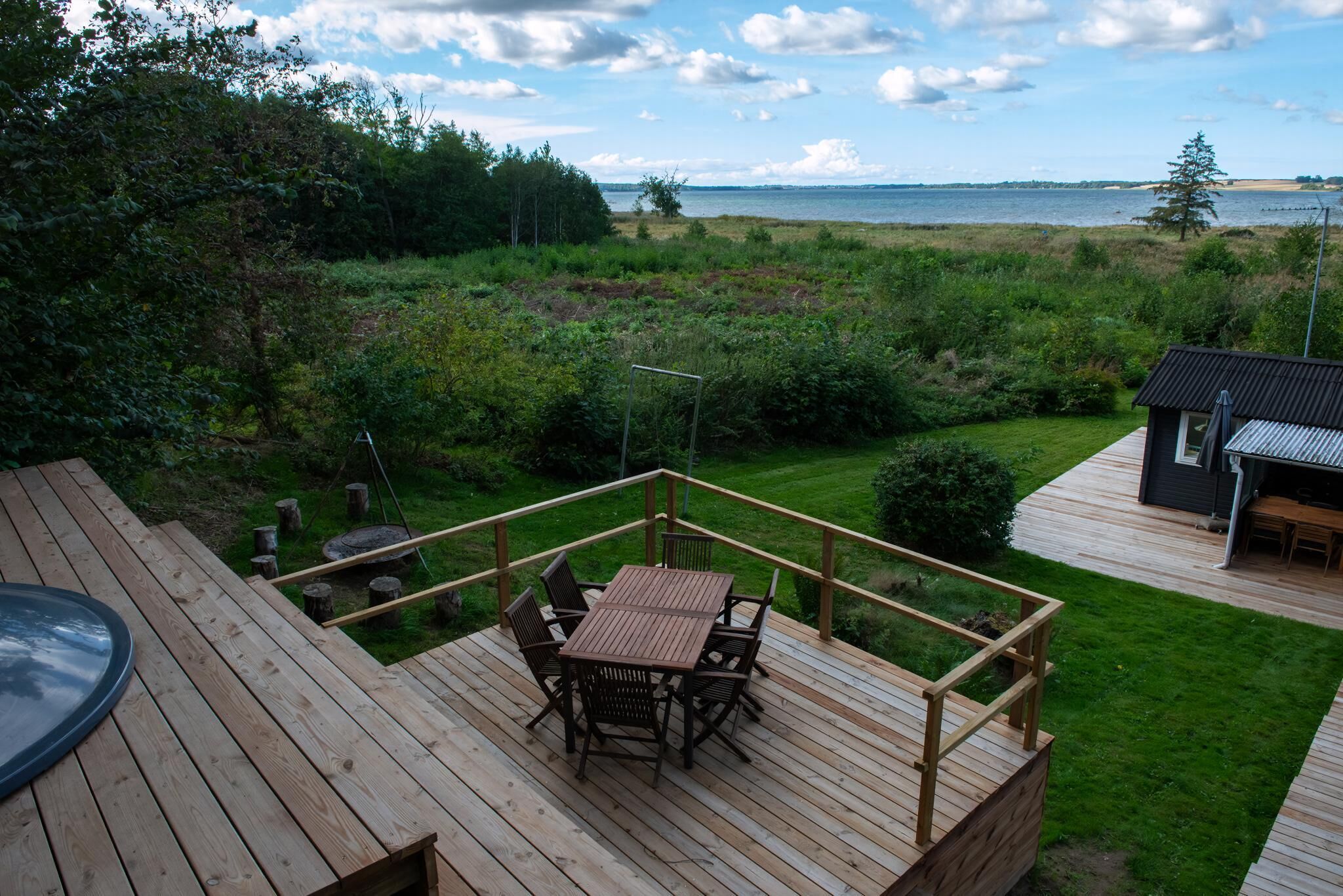 A wooden deck with a table and chairs, a small shed, and a view of a body of water.
