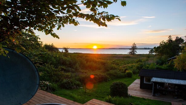 A deck with a grill, a small pool, and a view of the sunset over water. - Lovely cottage with wilderness bath and view (Holbæk)