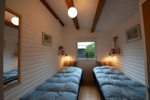Een kleine kamer met twee bedden, houten balken, een raam en wandlampen.