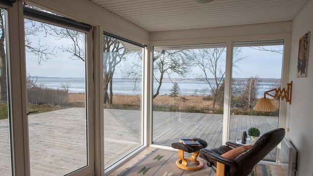 A room with large windows, a cushioned chair, and a small table. - Cottage with panoramic view of Lammefjorden (Holbæk)