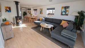 A modern living room with a sofa, coffee table, and a fireplace. There is a dining area with a table and chairs. - Cottage with panoramic view of Lammefjorden (Holbæk)