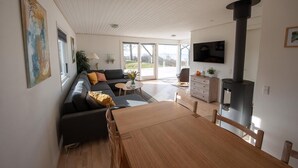 A modern living room with a sofa, dining table, and a wood-burning stove. - Cottage with panoramic view of Lammefjorden (Holbæk)
