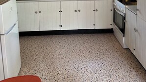 Une cuisine avec des meubles blancs, une fenêtre, une horloge et un évier.