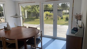 A dining area with a wooden table and chairs, a hanging light fixture, and a sliding glass door leading to a deck. - Summer house with outdoor sauna at Sjællands Odde (Sjællands Odde)