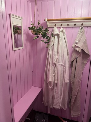 Et pink farvet værelse med en bænk, en hængende plante og håndklæder på en reol.