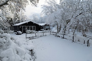 Une propriété enneigée comprenant une maison, une cour clôturée et des arbres couverts de neige.