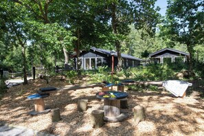 Une aire de jeux avec des structures en bois, une balançoire et un espace abrité avec un banc.