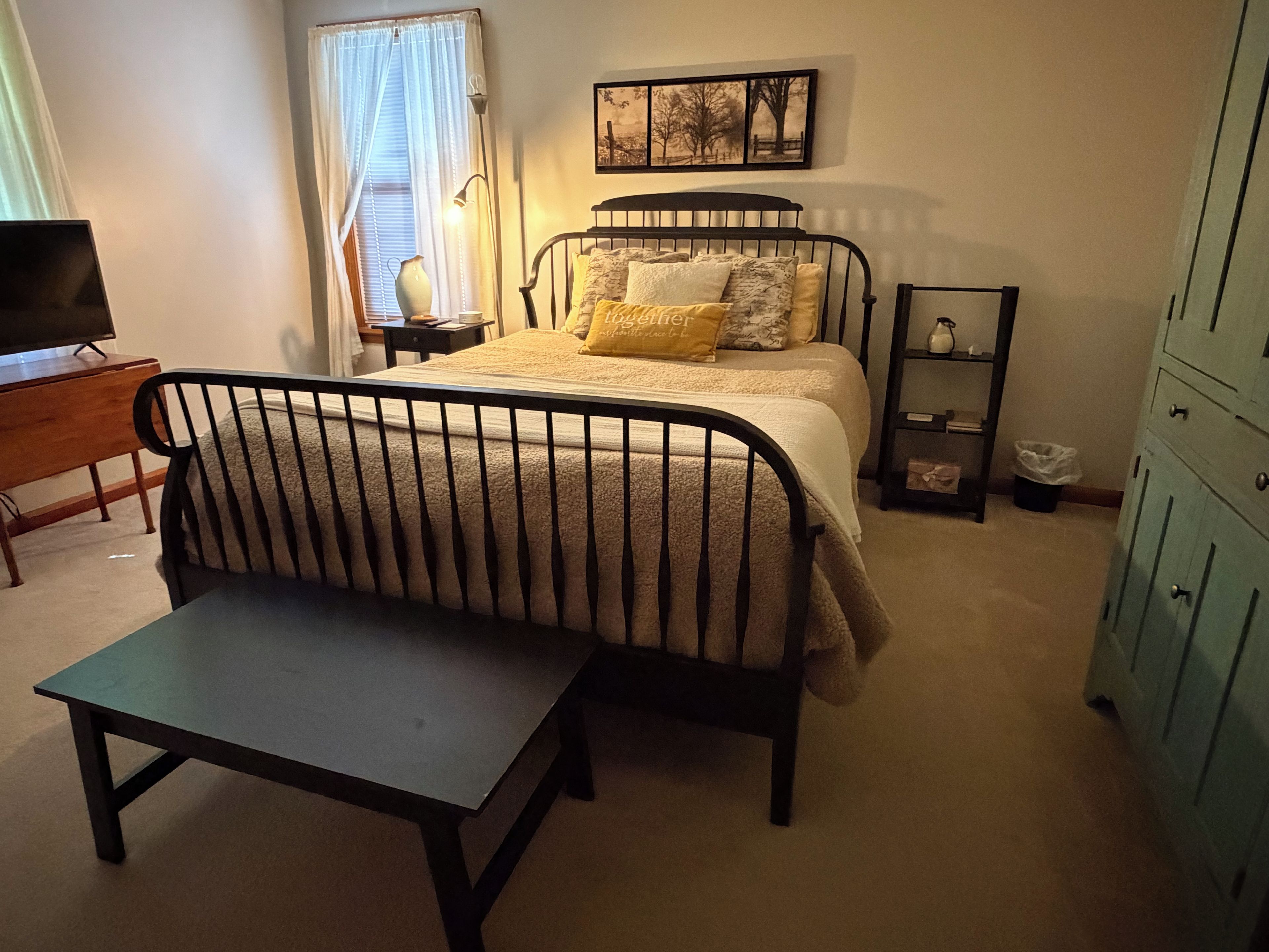 Een slaapkamer met een bed, nachtkastje, lamp, stoel, televisie en garderobe.