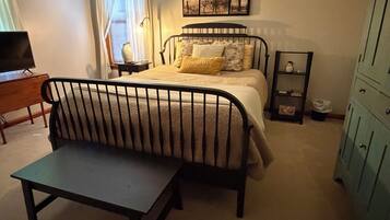 Een slaapkamer met een bed, nachtkastje, lamp, stoel, televisie en garderobe.