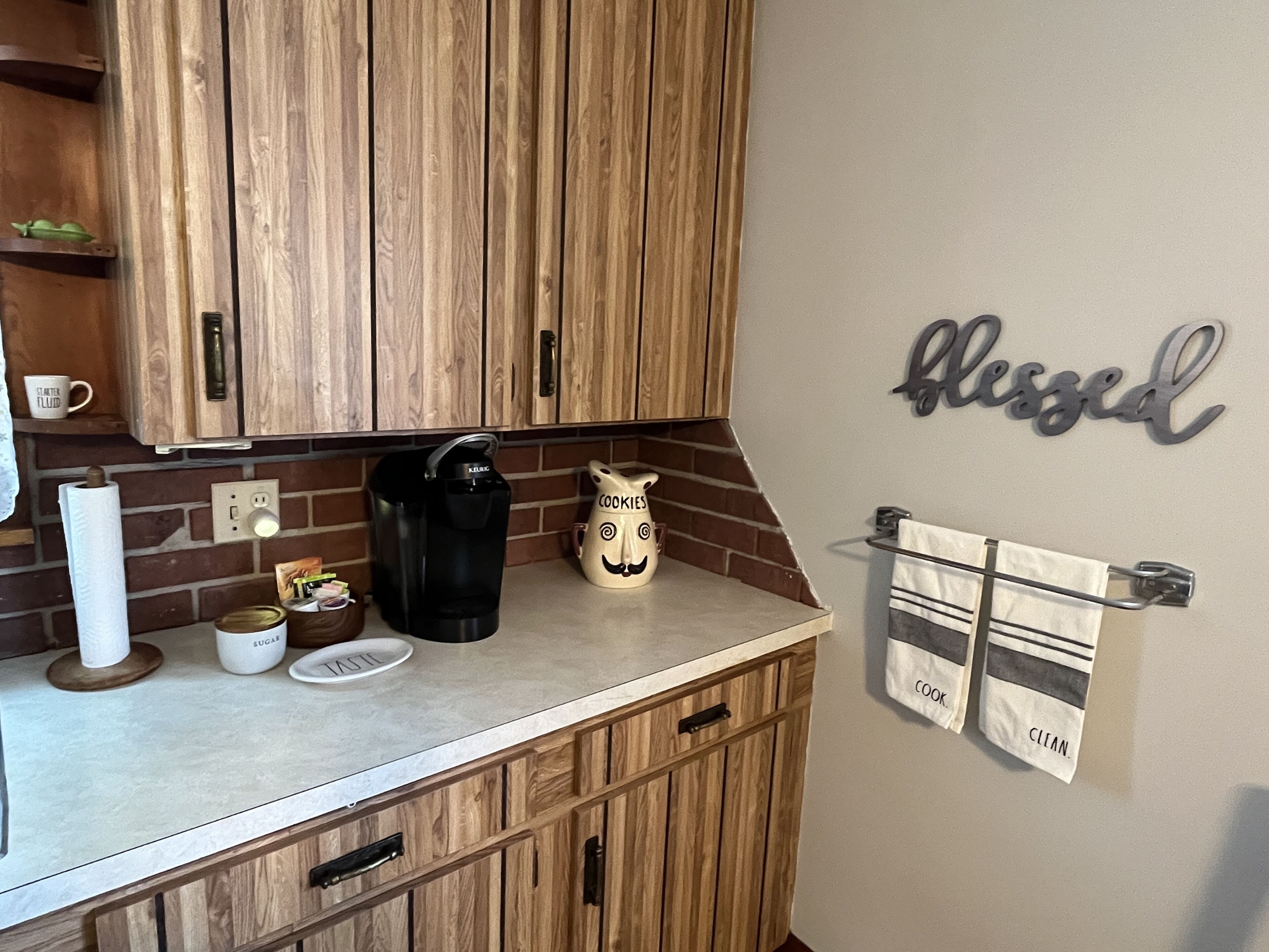 A kitchen with wooden cabinets, a kettle, a coffee maker, and a wall sign that says "blessed".