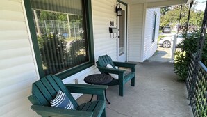 Un porche abrité avec deux fauteuils Adirondack verts et une petite table ronde, une boîte aux lettres et une porte portant le numéro 804.