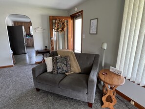Un salon avec un canapé gris, une petite table d’appoint en bois et une couronne décorative accrochée à la porte.