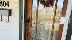 Une porte d’entrée en bois avec un panneau de verre, un paillasson et une guirlande décorative suspendue.