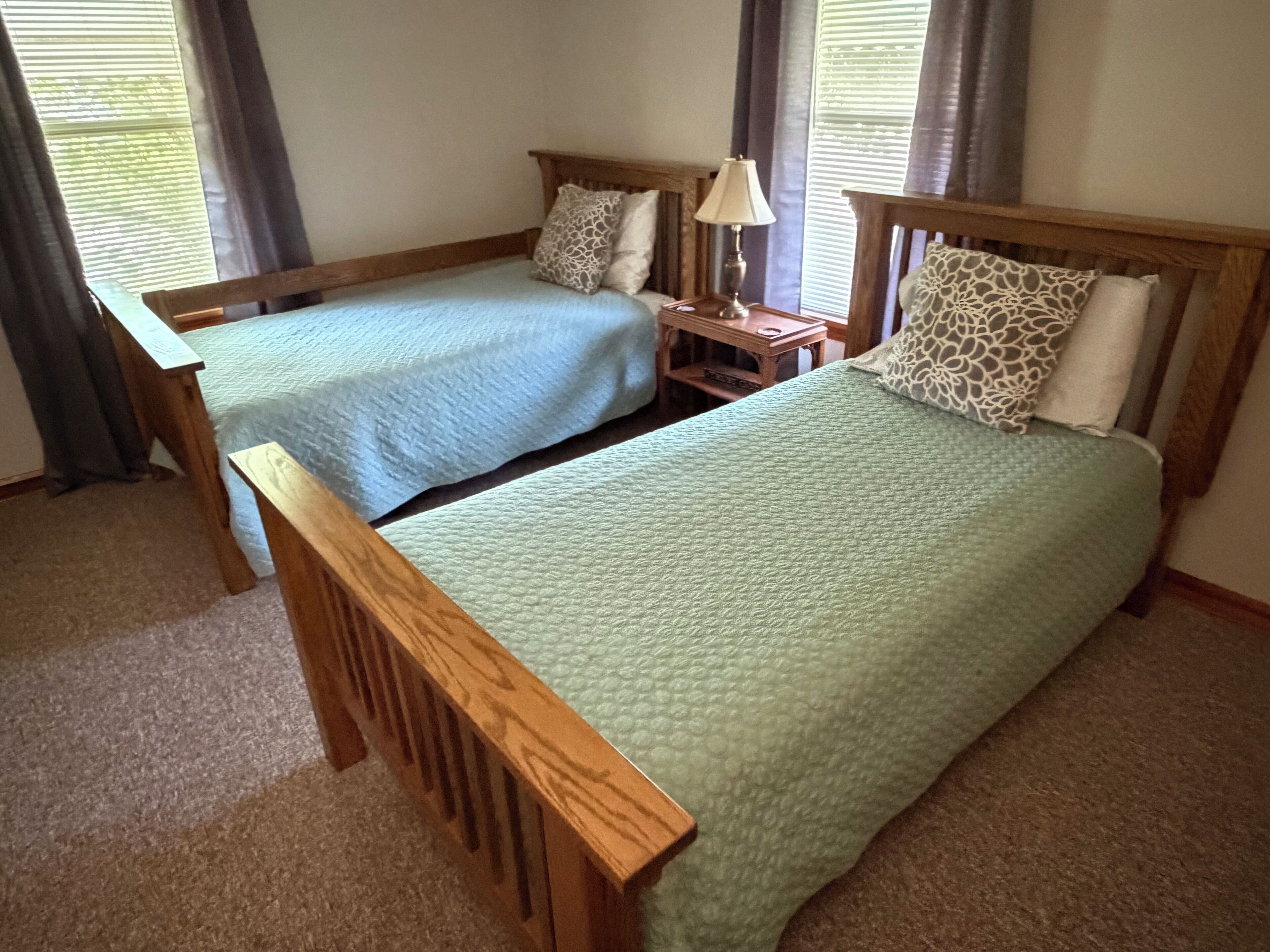 A bedroom with two single beds, a nightstand with a lamp, and a window with curtains.