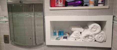 Un bany amb dutxa de vidre, un lavabo amb mirall i prestatges amb productes de tocador i tovalloles.