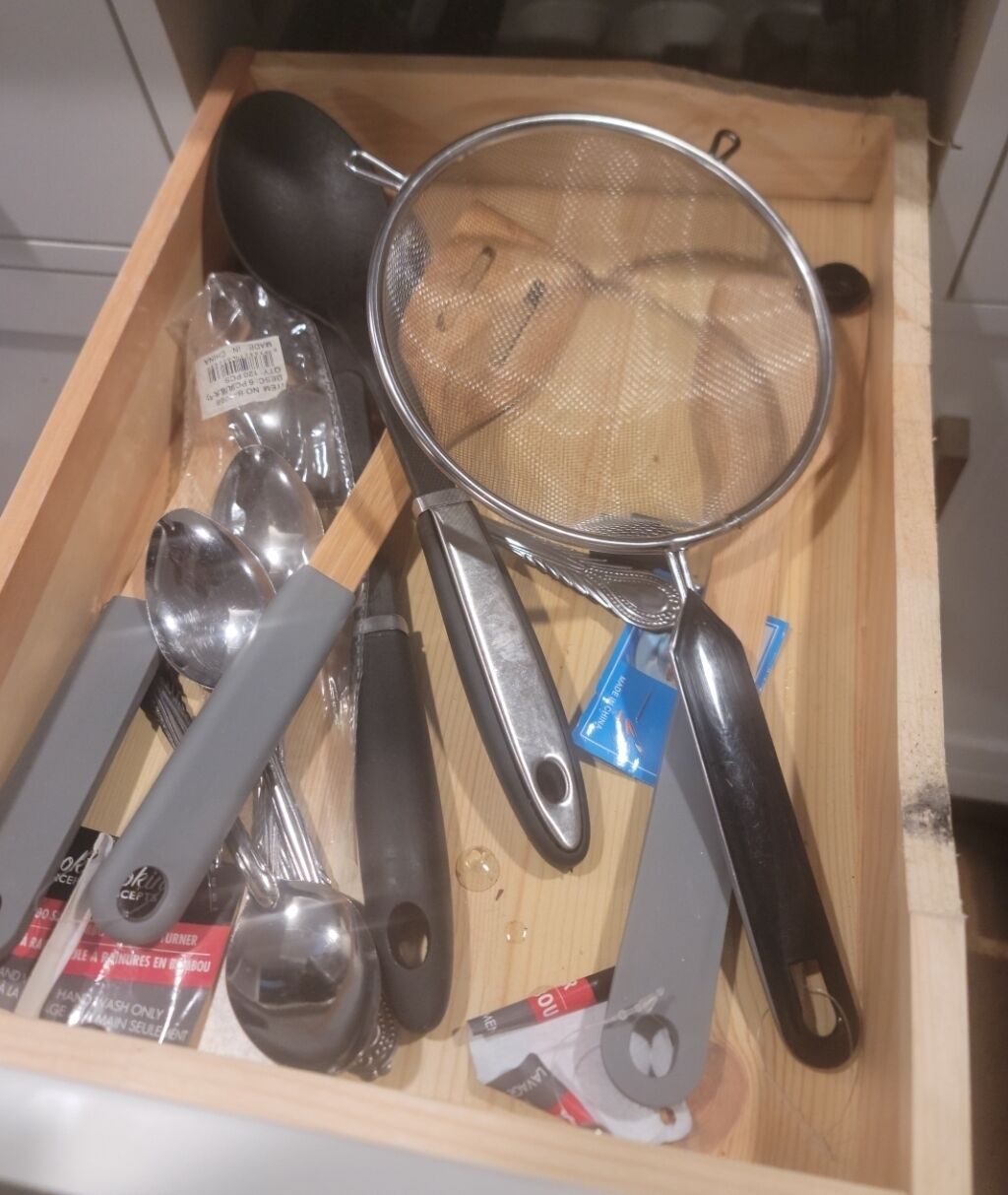 A drawer containing various kitchen utensils including spoons, a strainer, and a spatula.
