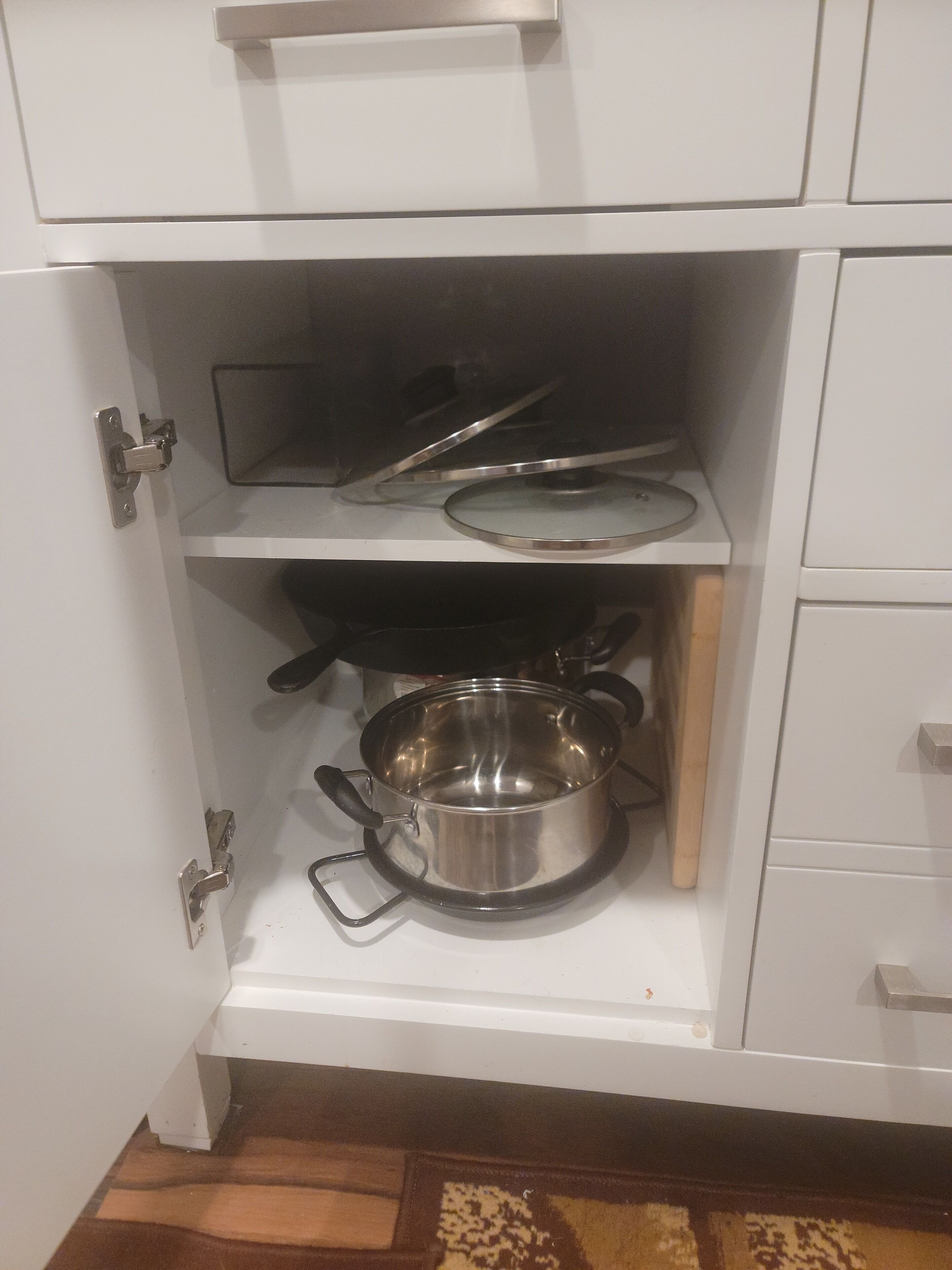 Une cuisine avec des meubles blancs, une casserole en acier inoxydable posée sur le plan de travail et une cuisinière.
