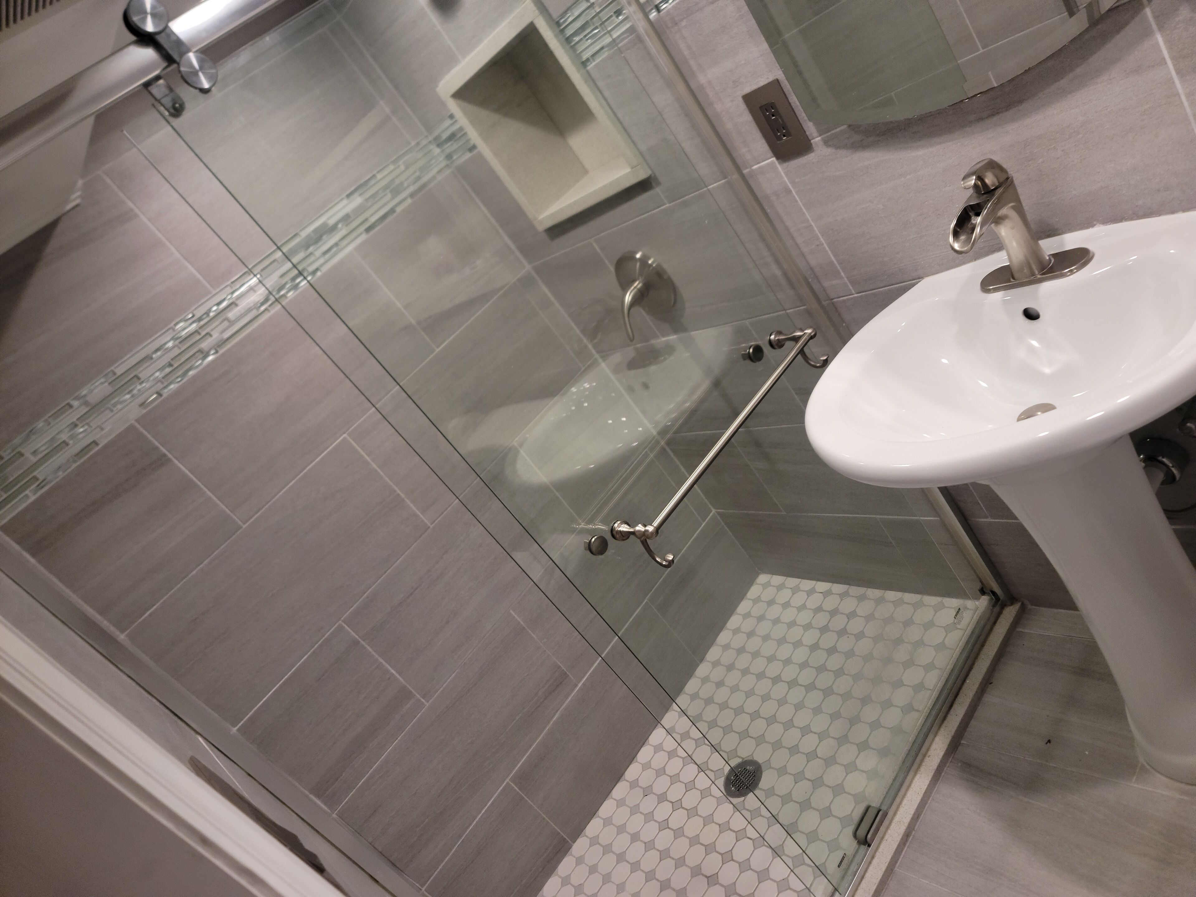 Ein modernes Badezimmer mit Duschkabine aus Glas, einem weißen Waschbecken und einer Glastür.