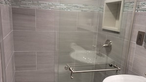 Moderni kylpyhuone, jossa on lasiseinällä varustettu suihku, valkoinen pesuallas ja laatoitetut seinät.