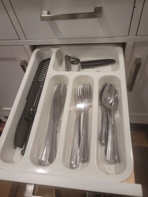 Un tiroir contenant des couverts soigneusement rangés, notamment un couteau, une fourchette, une cuillère et une râpe.