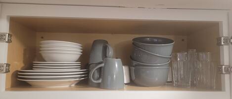 A cabinet with white plates, gray mugs, and clear glasses.