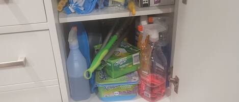 A storage cabinet with various cleaning supplies and a wastebasket.