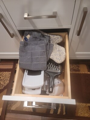 Un tiroir contenant des toilettes blanches, une paire de chaussons gris, un tapis de bain à motifs et une serviette rayée noire et blanche.