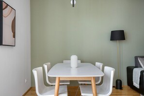 Un área de comedor moderna con una mesa y sillas blancas, una lámpara de pie y un sofá negro con una manta.